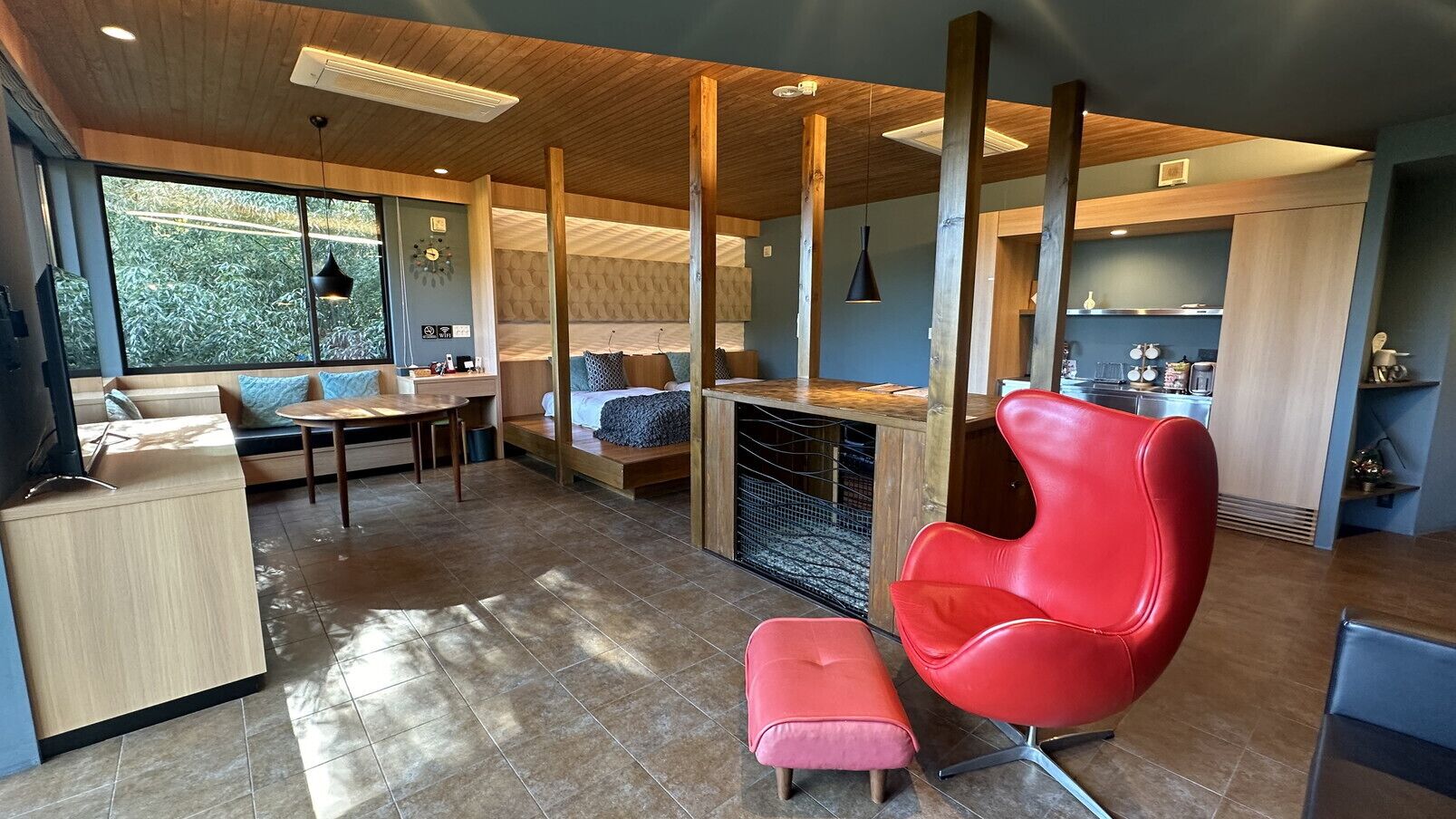 A modern kitchen with a dining area, a red chair, and a large window.