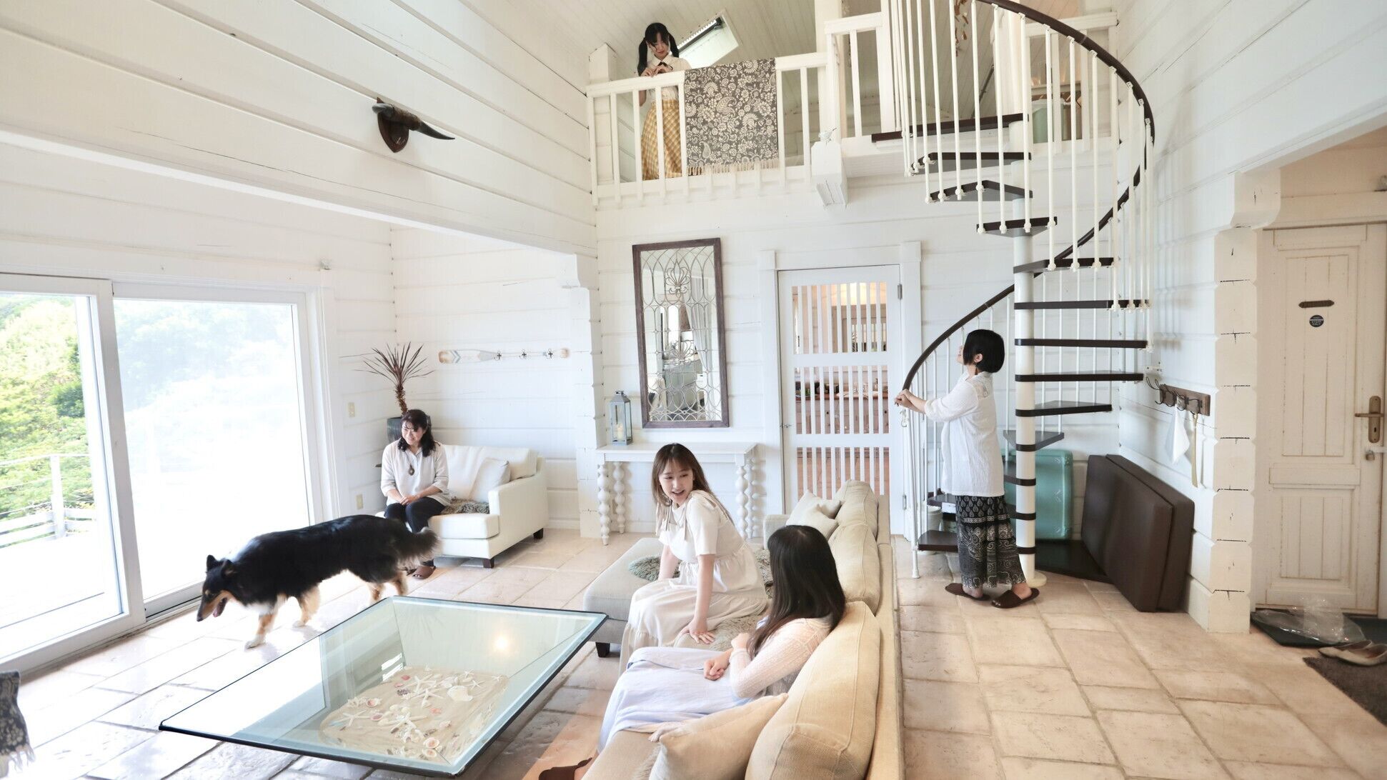 A spacious living room with a glass coffee table, a white staircase, and a view of the outdoors.