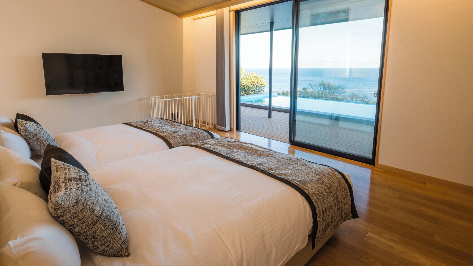 A modern bedroom with a large bed, a TV, and a view of the ocean.