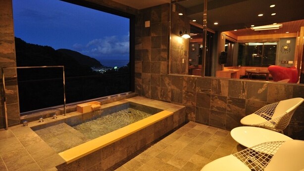 Un baño moderno con una bañera grande, una zona de estar y vistas a un paisaje urbano al atardecer.
