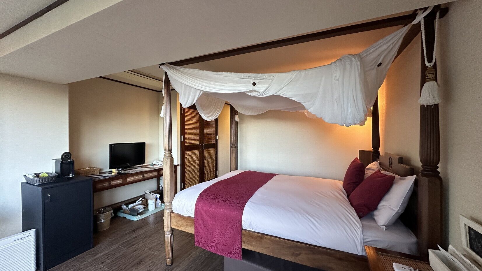 A four-poster bed with a canopy, a desk with a computer, and a wardrobe.