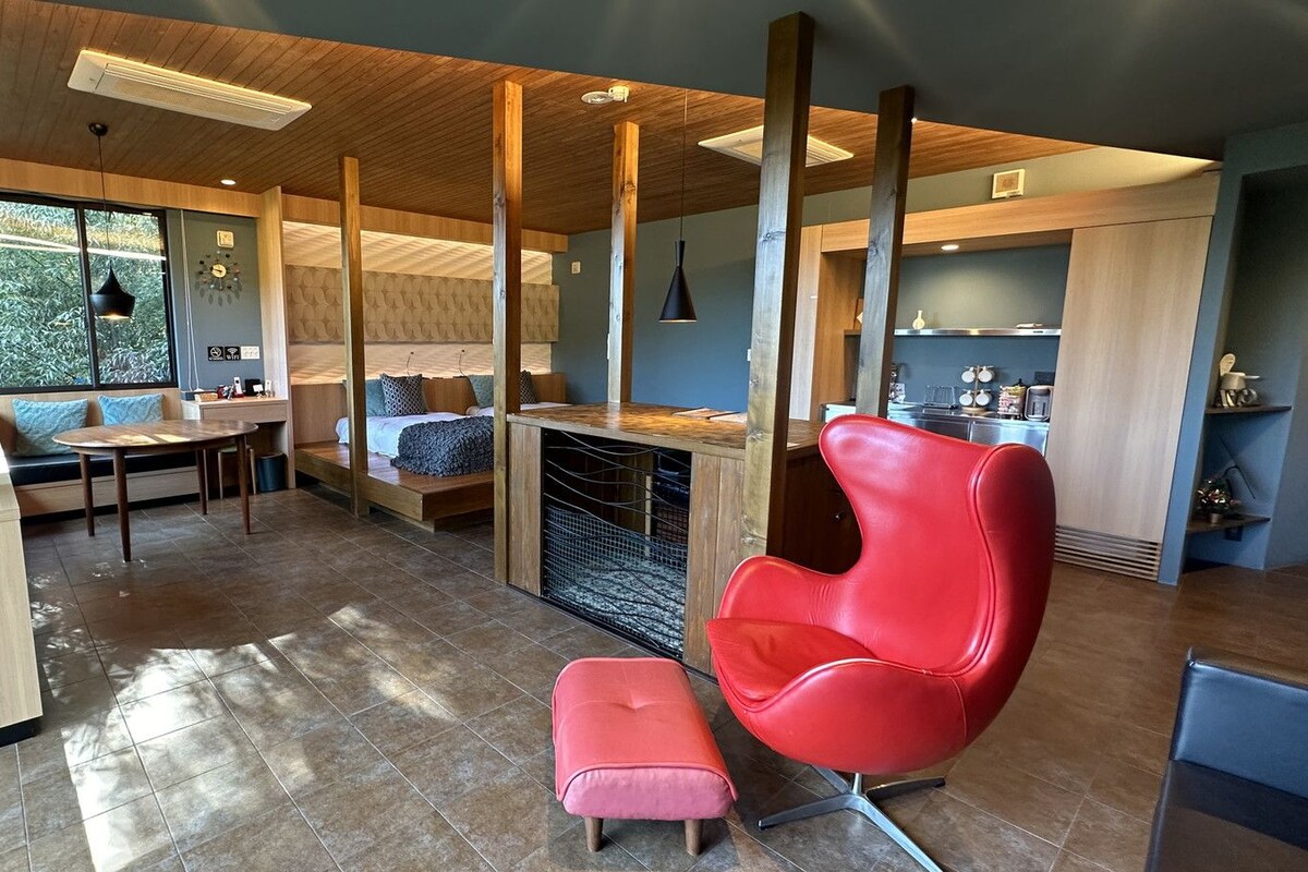 A modern kitchen with a dining area, a red chair, and a large window.