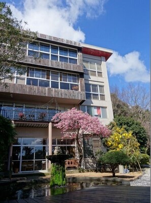 Un edificio a più piani con ampie finestre, un piccolo giardino con uno stagno e un ciliegio.