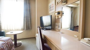 Een hotelkamer met een bed, een bureau met een computer, een telefoon en een raam met gordijnen.