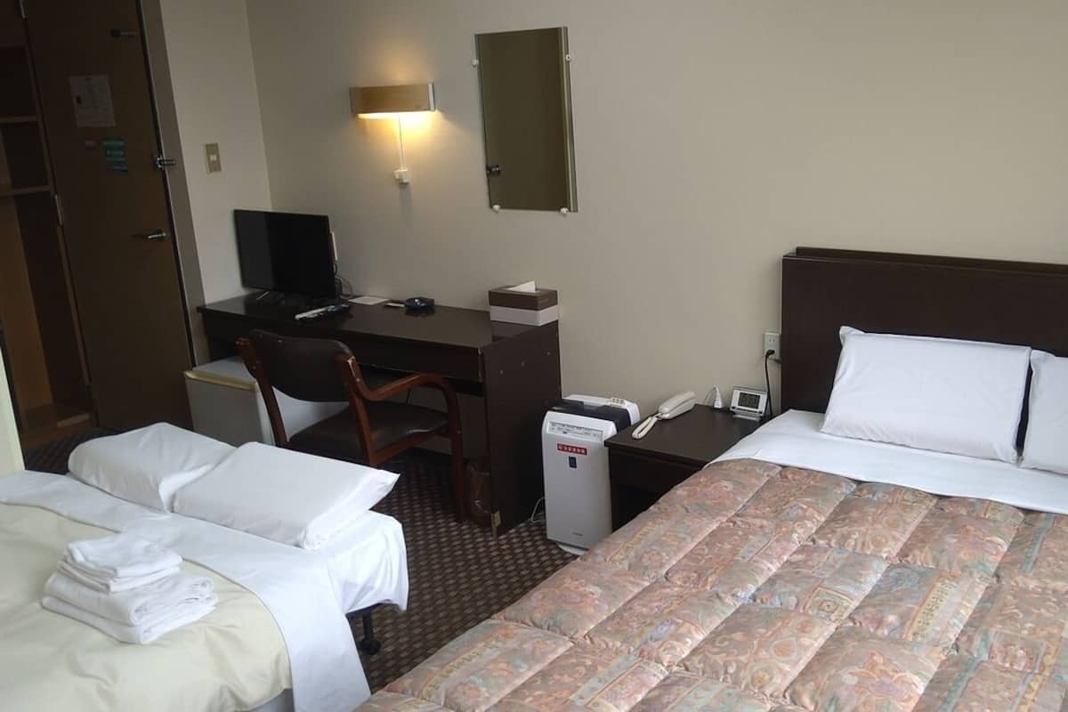 Ein Hotelzimmer mit zwei Betten, einem Schreibtisch mit Computer, einem Telefon und einem kleinen Schrank.