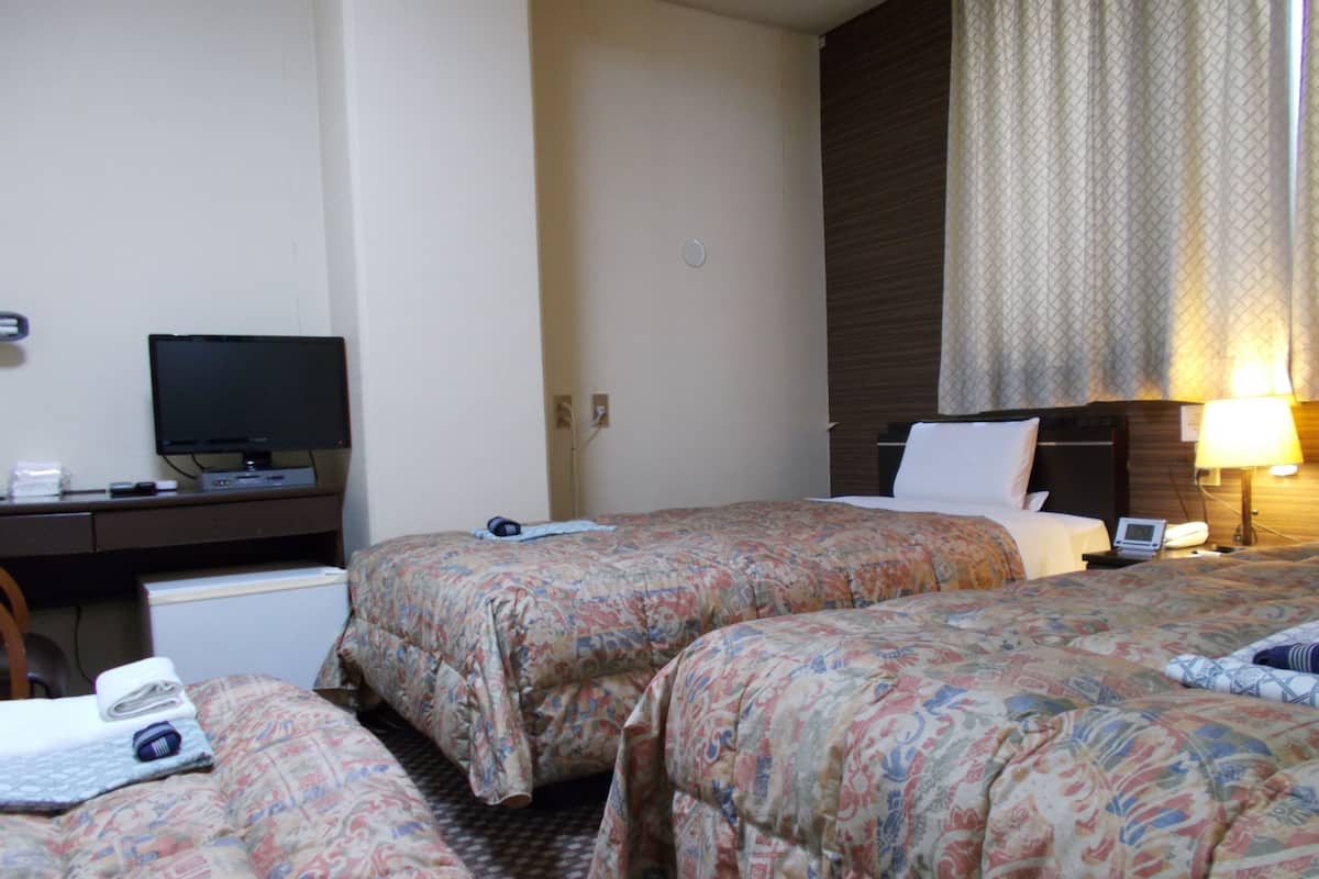 Ein Hotelzimmer mit zwei Betten, einem Schreibtisch mit Fernseher und einer Lampe.
