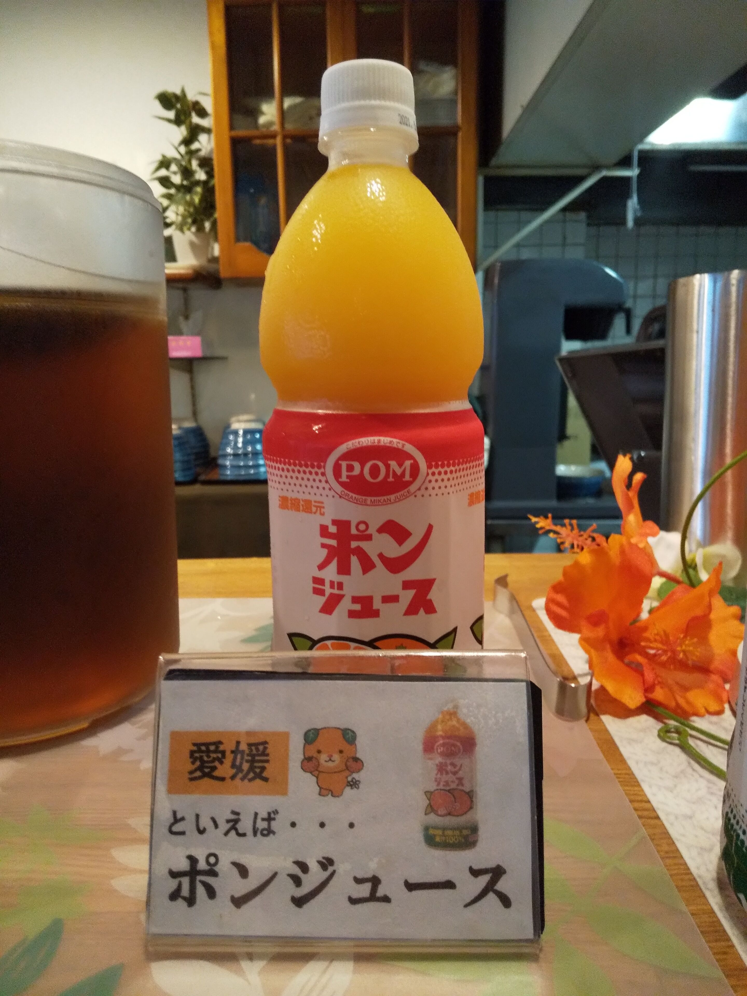 Een tafel met een fles sinaasappelsap, een theeglas en een bord met Japanse tekst.