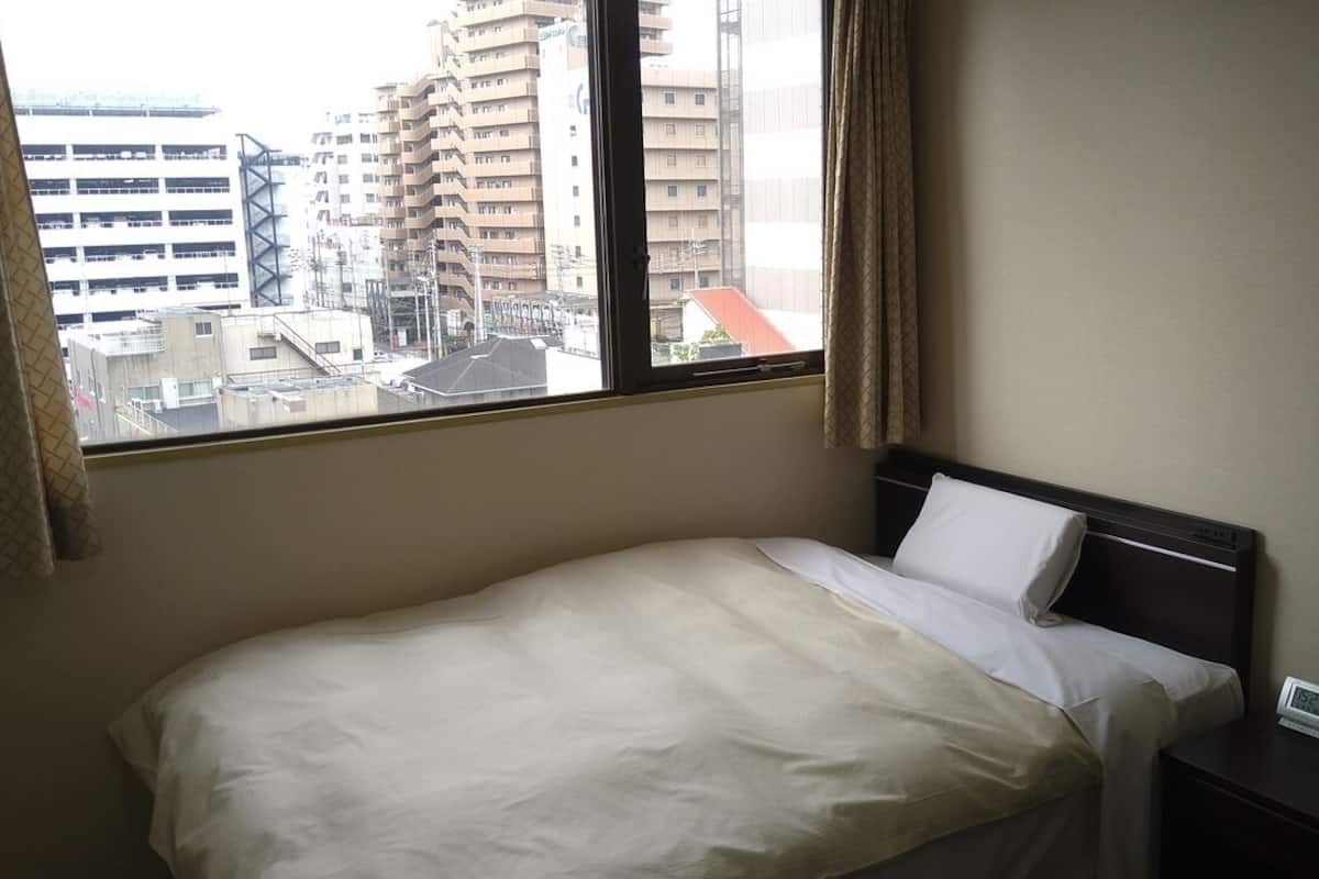 Ein Hotelzimmer mit Bett, Nachttisch mit Uhr und Fenster mit Blick auf die Stadt.