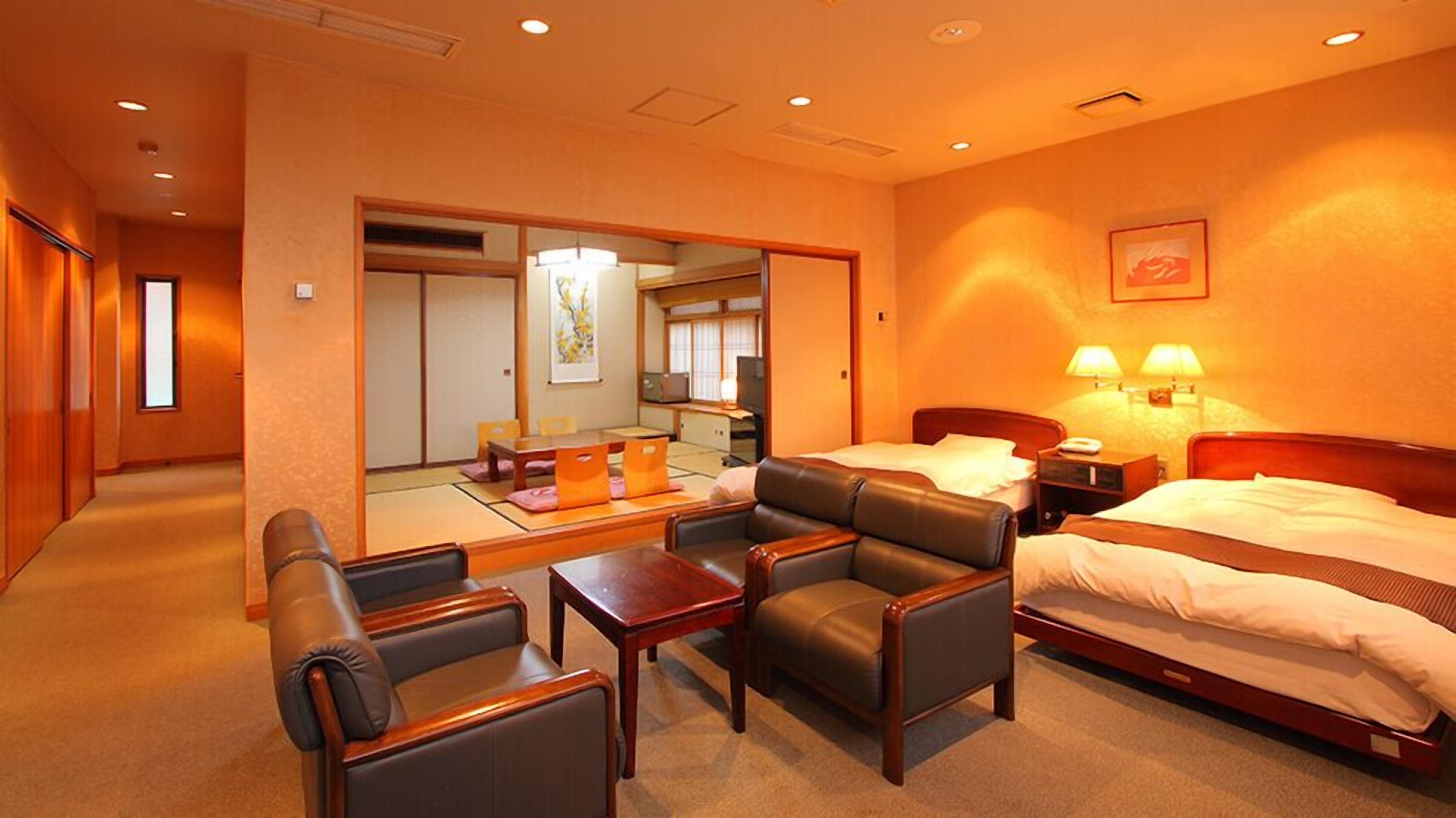 Ein Hotelzimmer mit einem Bett, zwei Nachttischen, einem Schreibtisch, einem Sessel und einer Sitzecke mit Kissen.