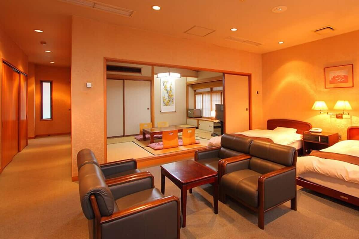 Une chambre d’hôtel comprenant un lit, deux tables de chevet, un bureau, une chaise et un coin salon avec des coussins.