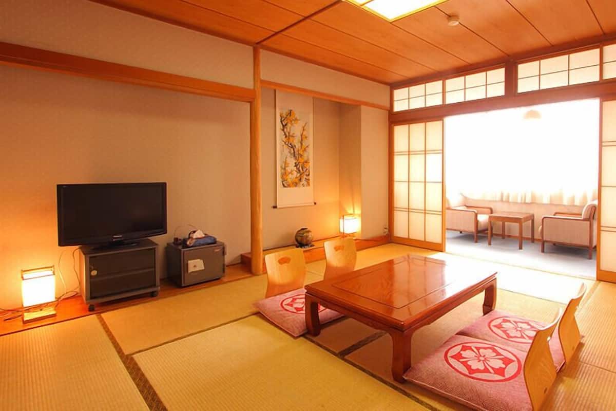 Une pièce de style japonais traditionnel, avec un sol recouvert de tatamis, une télévision, un meuble, une table et un ensemble de canapés.