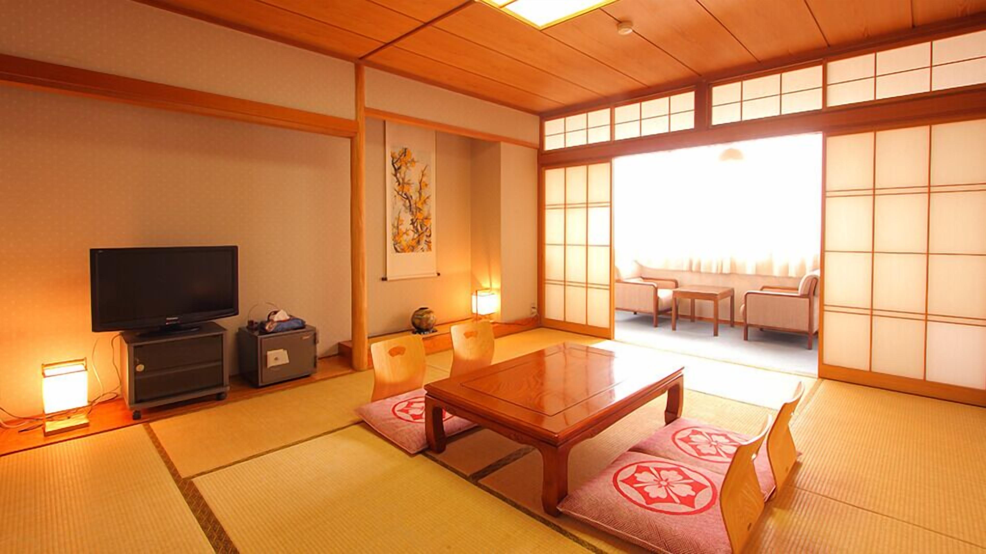 Une pièce de style japonais traditionnel, avec un sol recouvert de tatamis, une télévision, un meuble et une porte coulissante donnant sur un espace salon.