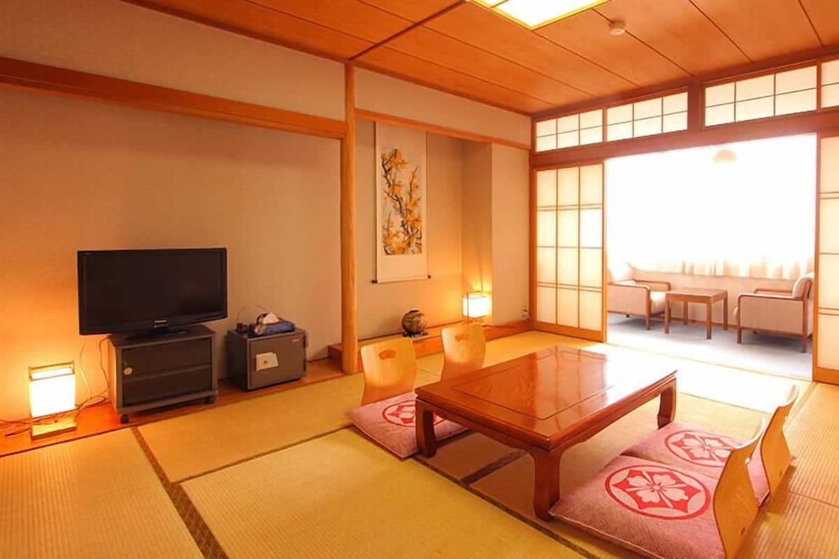Une pièce de style japonais traditionnel, avec un sol recouvert de tatamis, une télévision, un meuble et une porte coulissante donnant sur un espace salon.