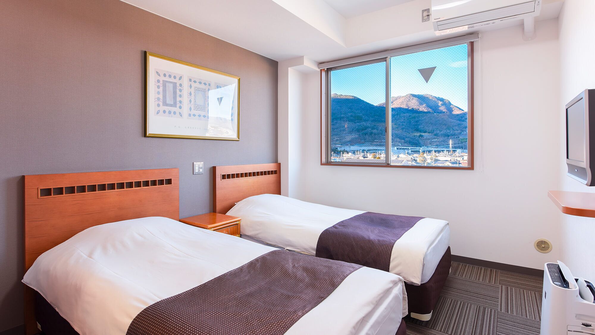 Une chambre d’hôtel avec deux lits, une fenêtre donnant sur la montagne, un tableau encadré au mur et un bureau avec une imprimante.