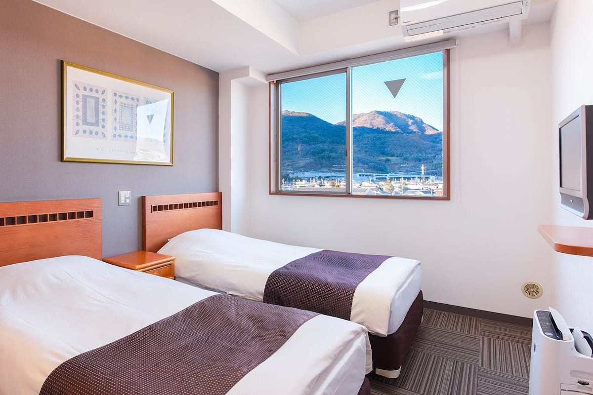 Une chambre d’hôtel avec deux lits, une fenêtre donnant sur la montagne, un tableau encadré au mur et un bureau avec une imprimante.