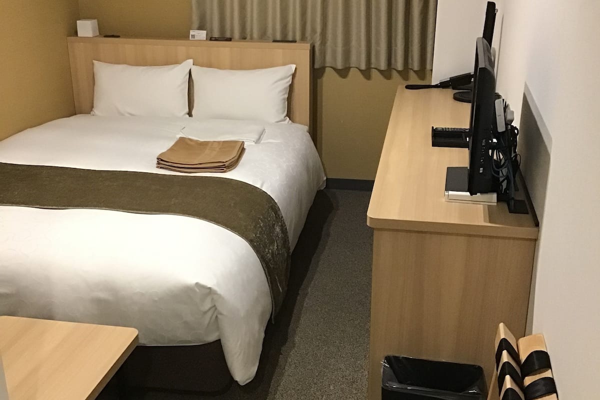 A hotel room with a bed, a desk, a chair, a TV, and a window with curtains.