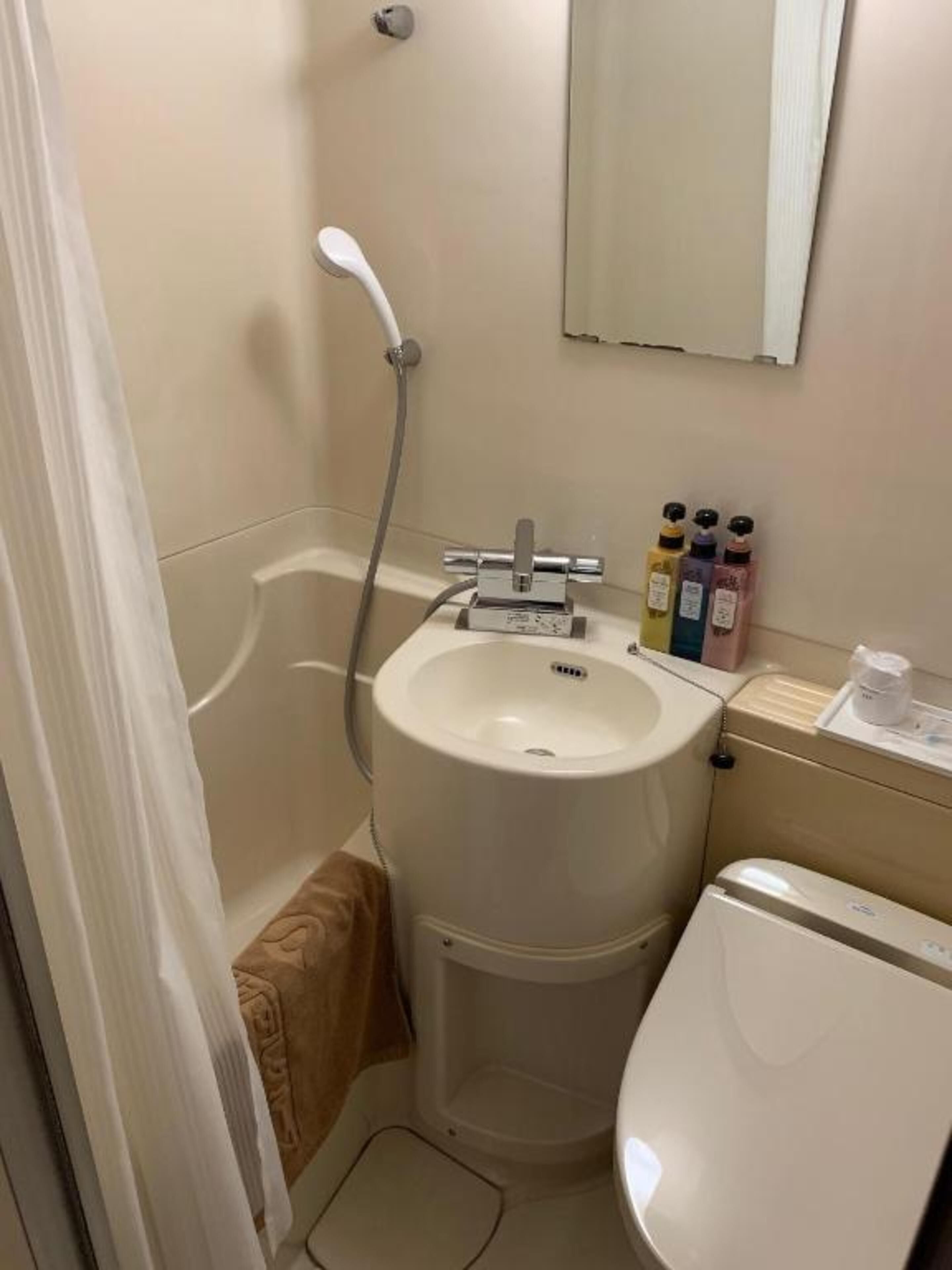 A small bathroom with a toilet, sink, and shower. There are toiletries on the sink counter.