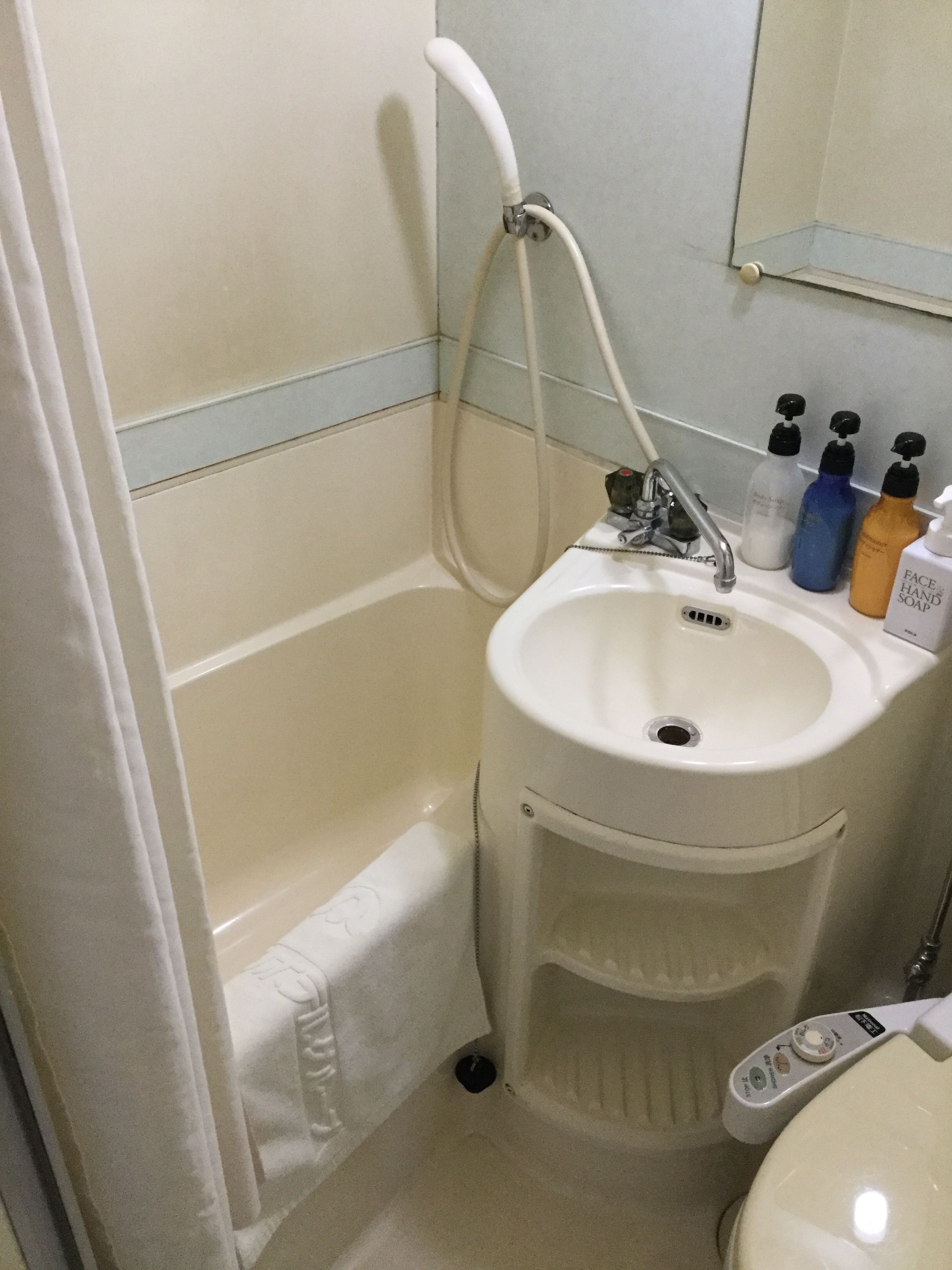 Een badkamer met een bad, een wastafel en drie flessen handzeep.