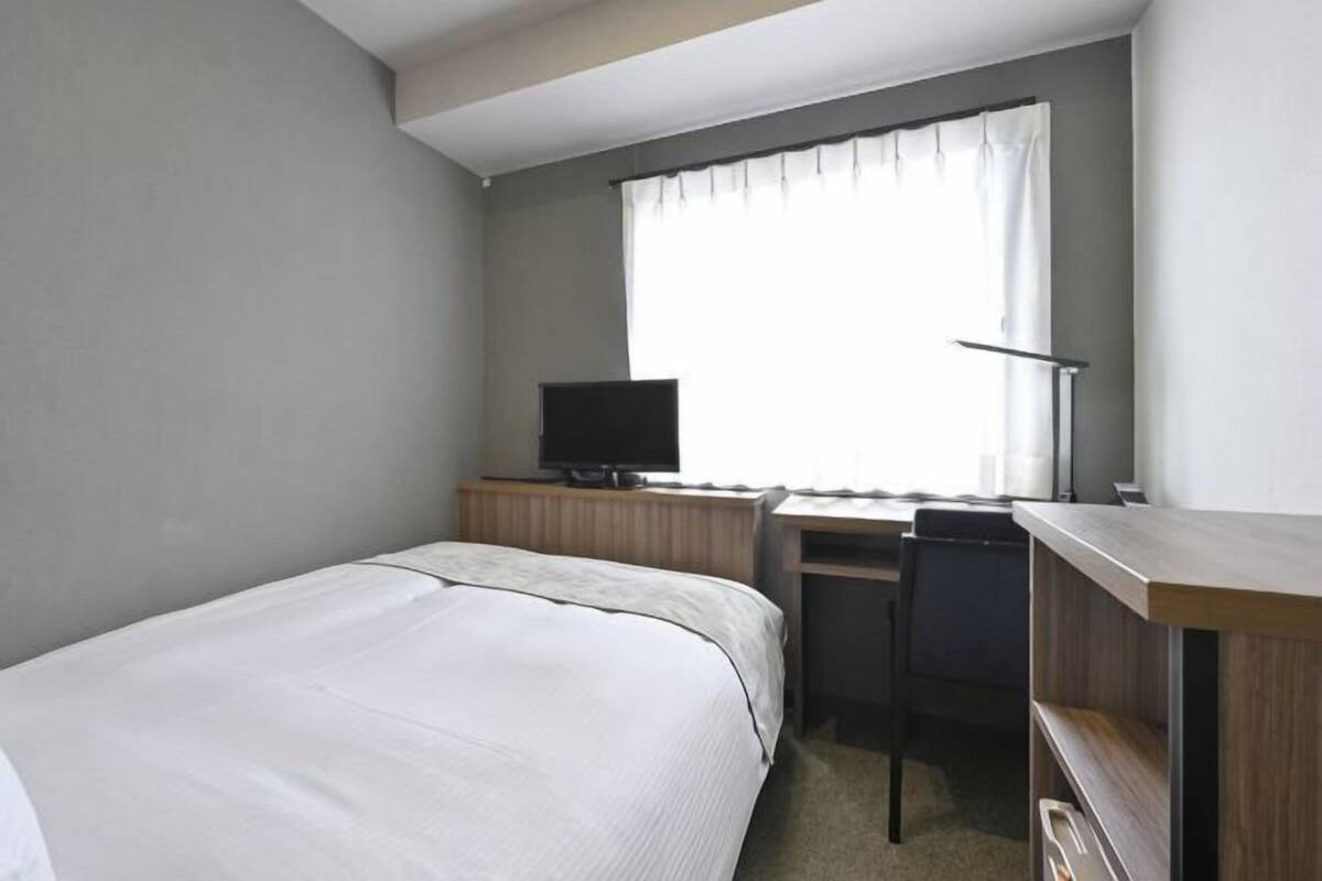 A hotel room with a bed, a desk, a television, and a window with curtains.