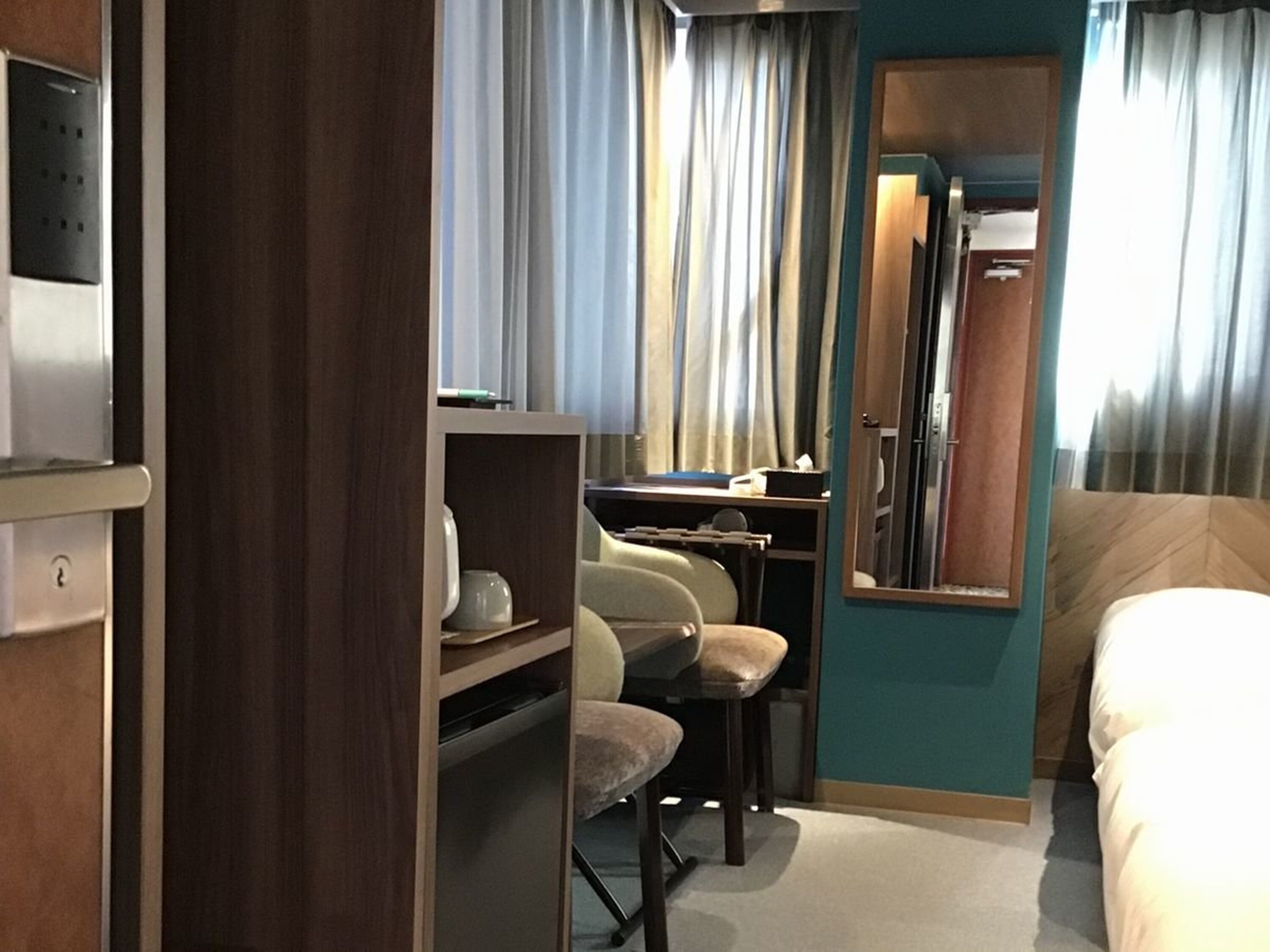 Ein Hotelzimmer mit Bett, Schreibtisch, Stuhl, Spiegel und Kleiderschrank.