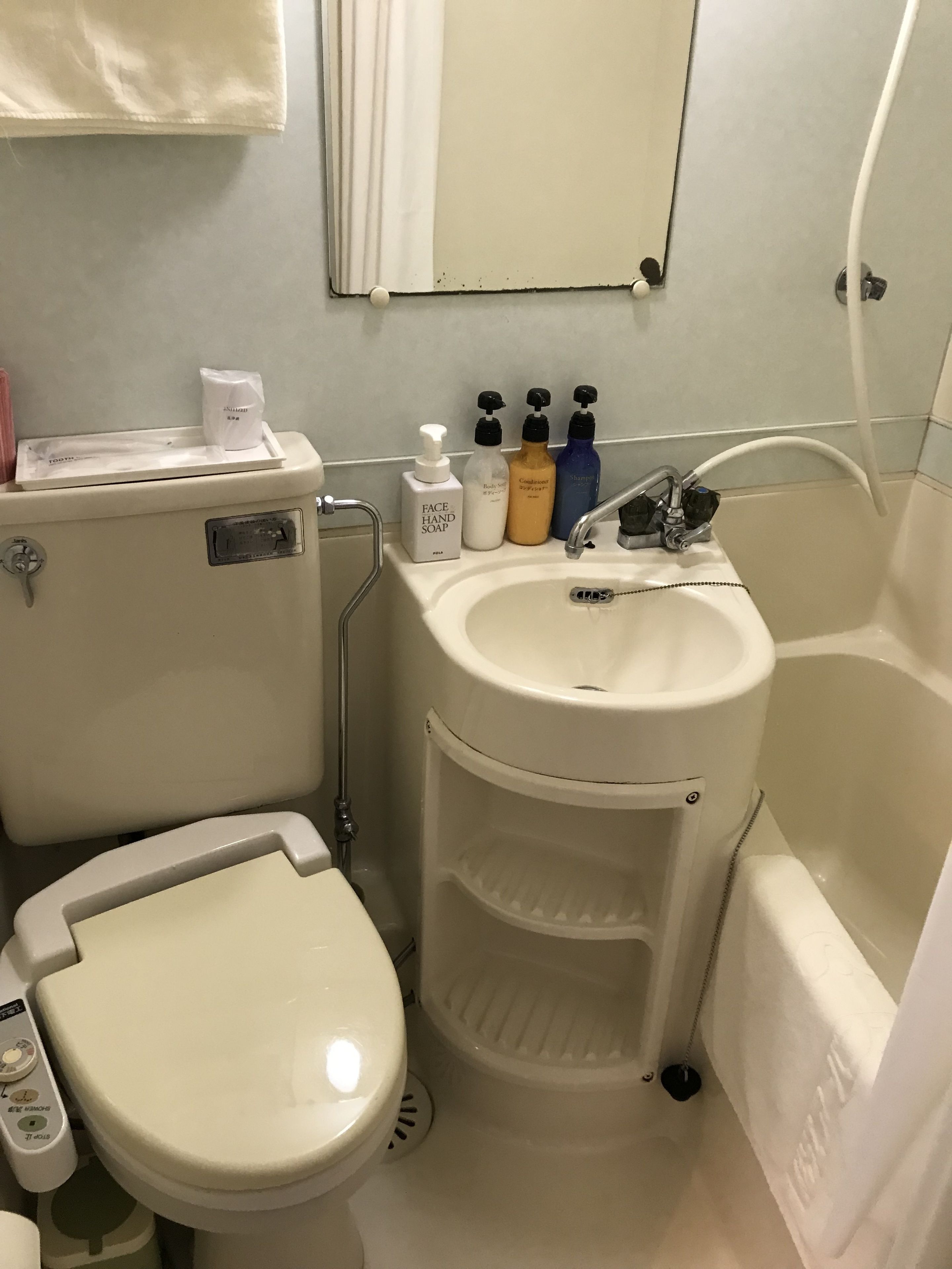 Un baño con inodoro, lavamanos y bañera. Hay artículos de aseo en el lavamanos y un espejo encima.