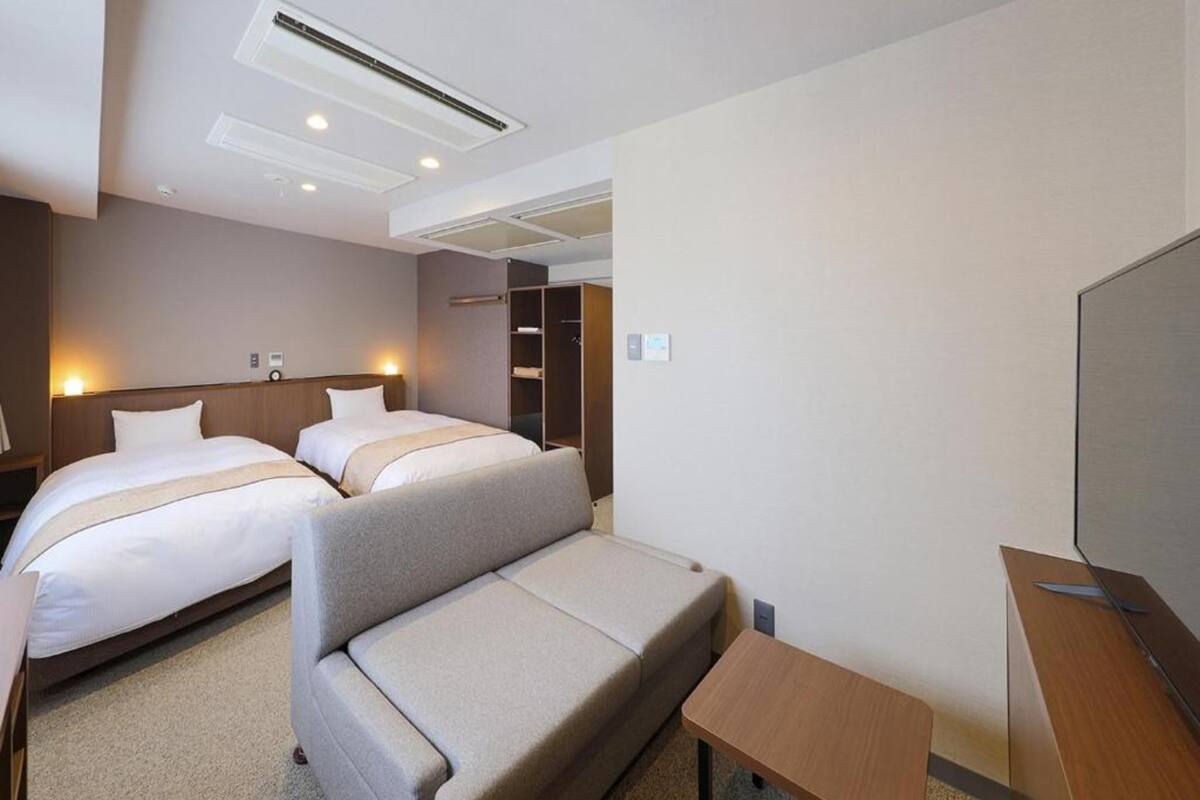 A hotel room with two beds, a sofa, a TV, and a wardrobe.