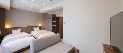 Habitación de hotel con dos camas, un sofá, un televisor y un armario.