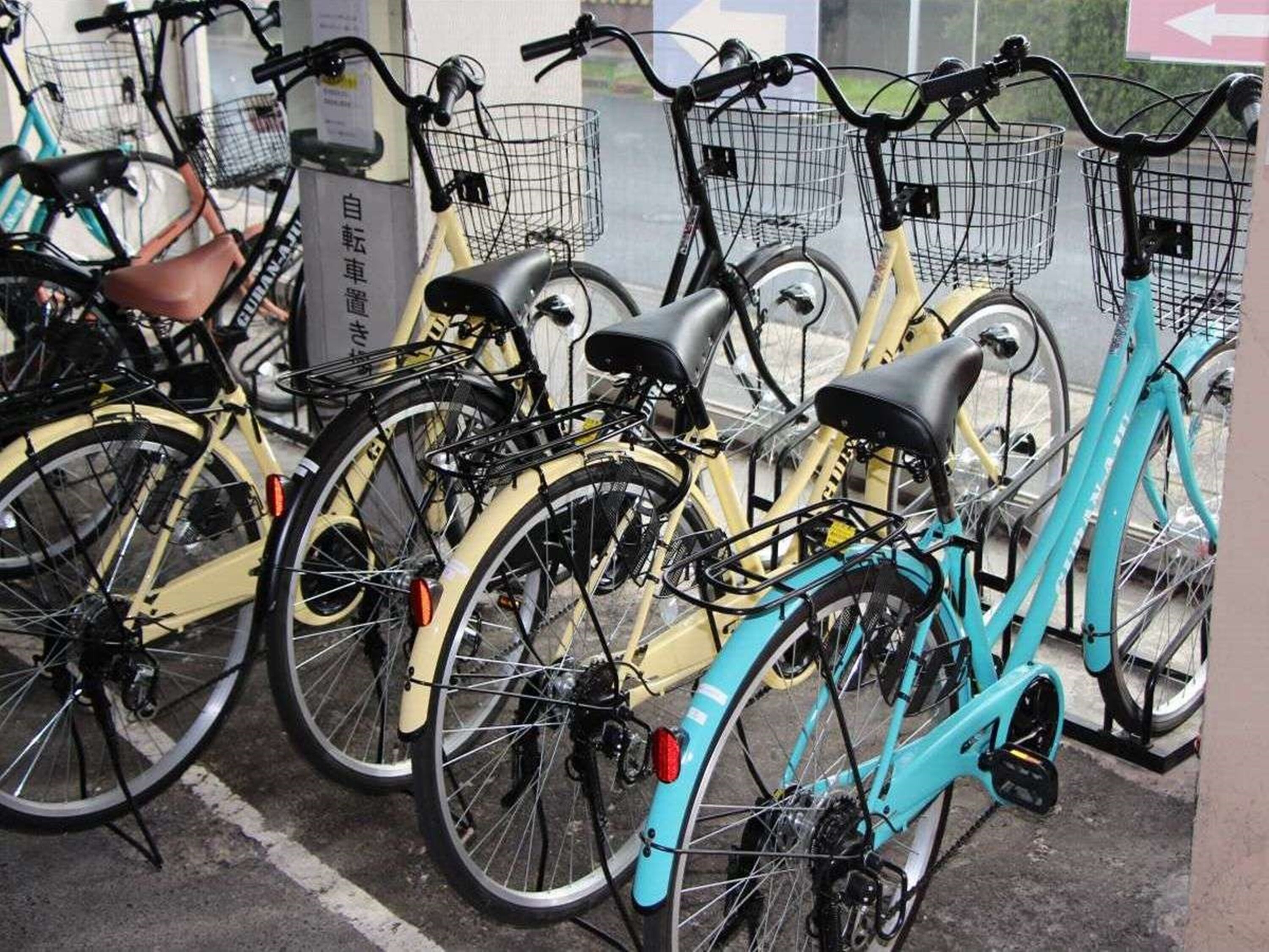 Une rangée de vélos est stationnée dans un espace prévu à cet effet, probablement une station de vélos en libre-service, et un panneau indique la direction à suivre.