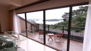 Un balcon avec vue sur un pont et sur l’eau, un plancher en bois et deux chaises.