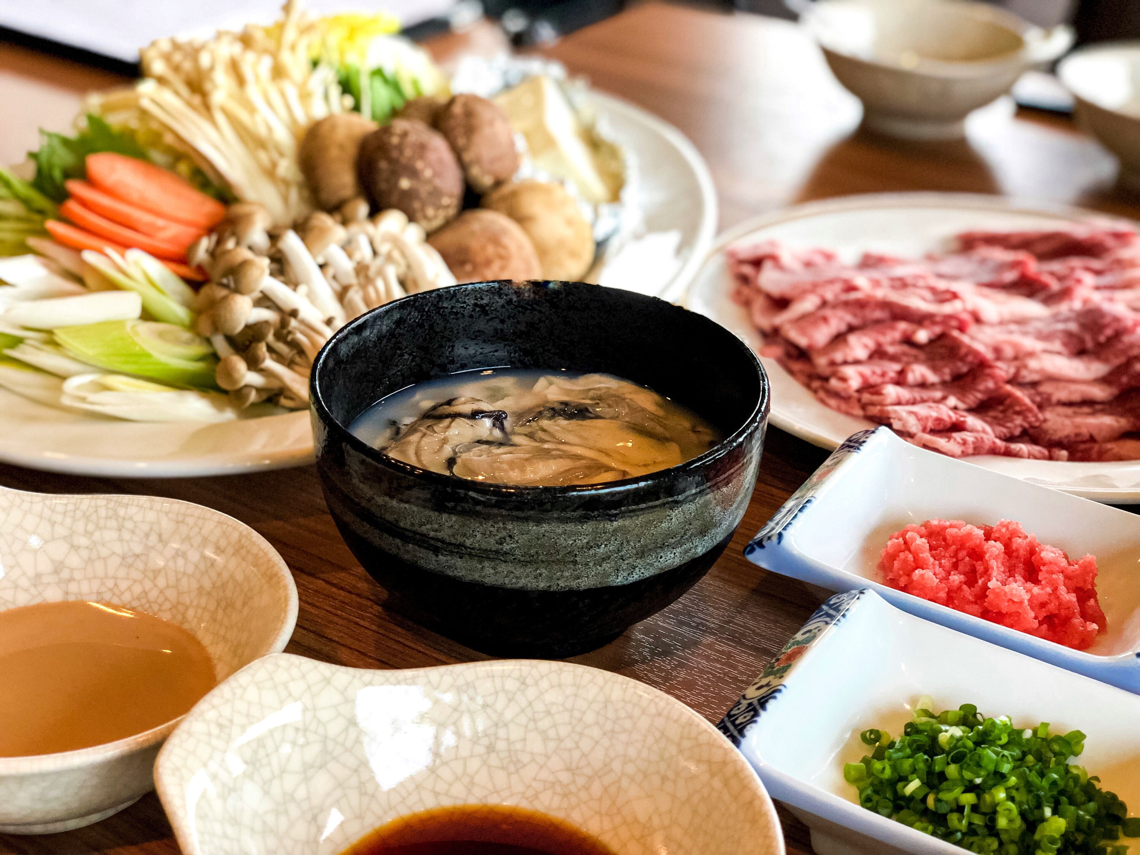 Una variedad de platos, incluyendo un tazón de sopa, carne en rodajas, verduras y una fuente de vegetales encurtidos.