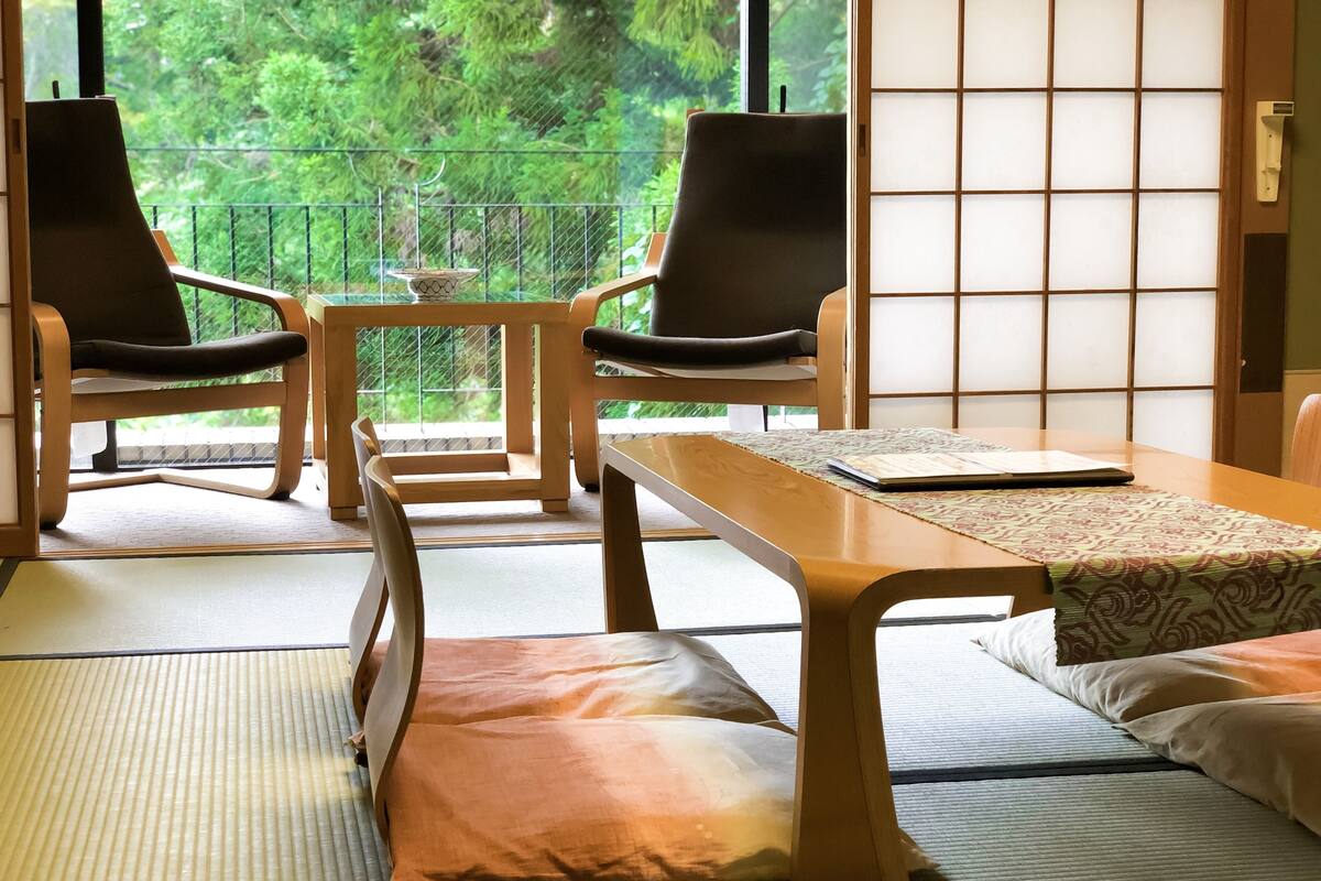 A traditional Japanese room with tatami flooring, a low table, two chairs, and a sliding shoji screen.