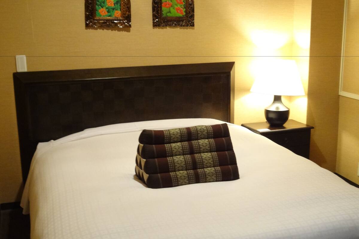 A neatly made bed with a patterned pillow, a bedside lamp, and two framed floral pictures on the wall.