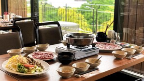 Une table à manger, dressée avec différents plats, et un réchaud portable, le tout installé devant un paysage pittoresque comprenant un lac et une végétation luxuriante.