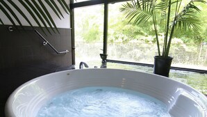 Un bain à remous doté d’un panneau de commande, une fenêtre donnant sur un paysage verdoyant et une plante en pot.