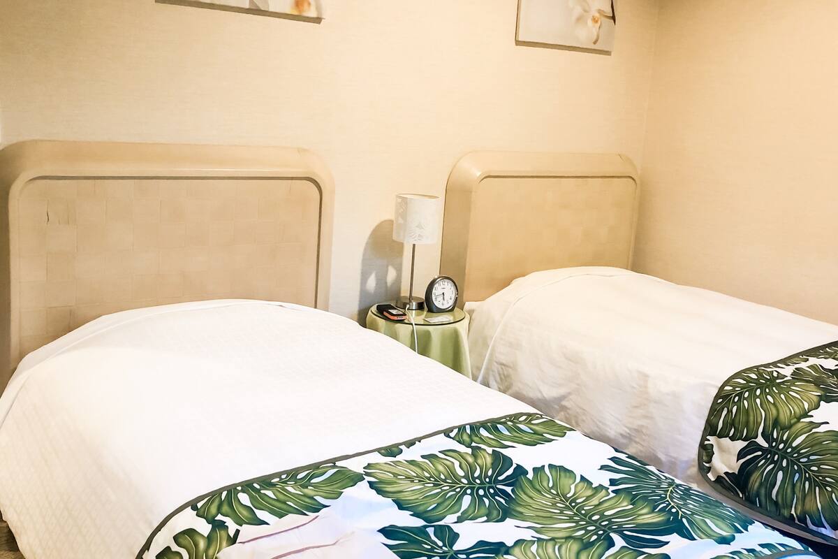 A hotel room with two beds, a nightstand with a lamp and clock, and artwork on the walls.