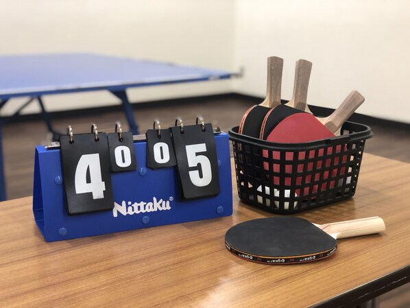 A table with a Nittaku table tennis paddle, a paddle basket with table tennis balls, and a score display.