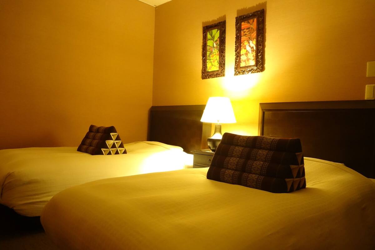 A hotel room with two beds, each with a unique pillow design, a nightstand with a lamp, and two wall-mounted picture frames.