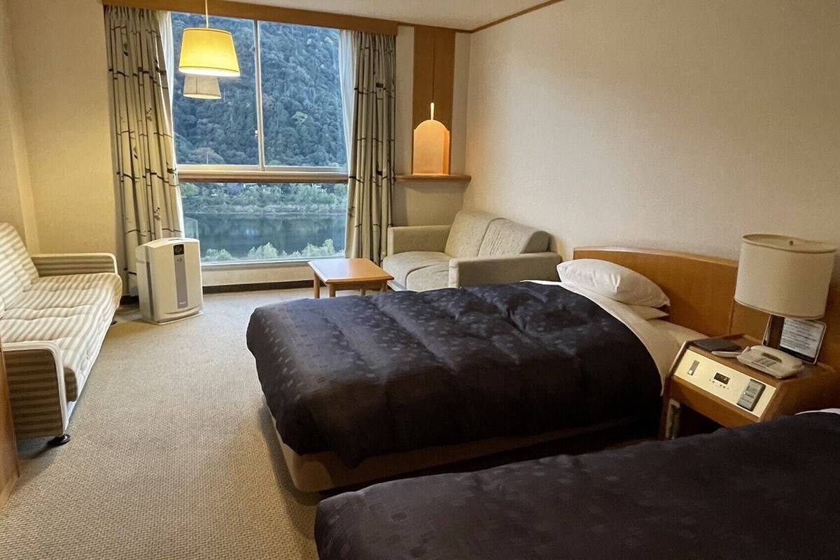 Et hotelværelse med to senge, en sofa, et skrivebord, en lampe og udsigt til en sø.
