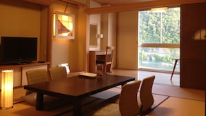 A modern dining area with a large table, chairs, a television, and a view of a forest through a large window. - Gifu Grand Hotel (Gifu)