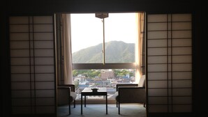 A room with tatami flooring, a low table, two chairs, and a view of a town and mountains through a large window with sliding doors. - Gifu Grand Hotel (Gifu)
