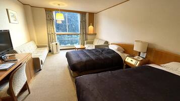 Une chambre d’hôtel avec deux lits, un bureau avec un ordinateur, une chaise, une lampe et une fenêtre donnant sur des arbres.