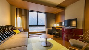 A modern hotel room with a sofa, a small round table, a TV, and a view of the mountains through the window. - Gifu Grand Hotel (Gifu)