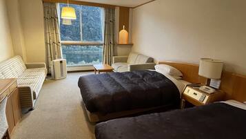 Une chambre d’hôtel avec deux lits, un canapé, une petite table, une lampe et une vue sur un lac par la fenêtre.
