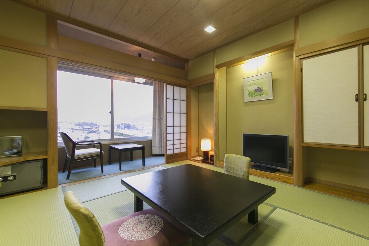Et traditionelt japansk rum med tatamimåtter, et lavt bord, et fjernsyn og skydedøre, der fører ud til en balkon.