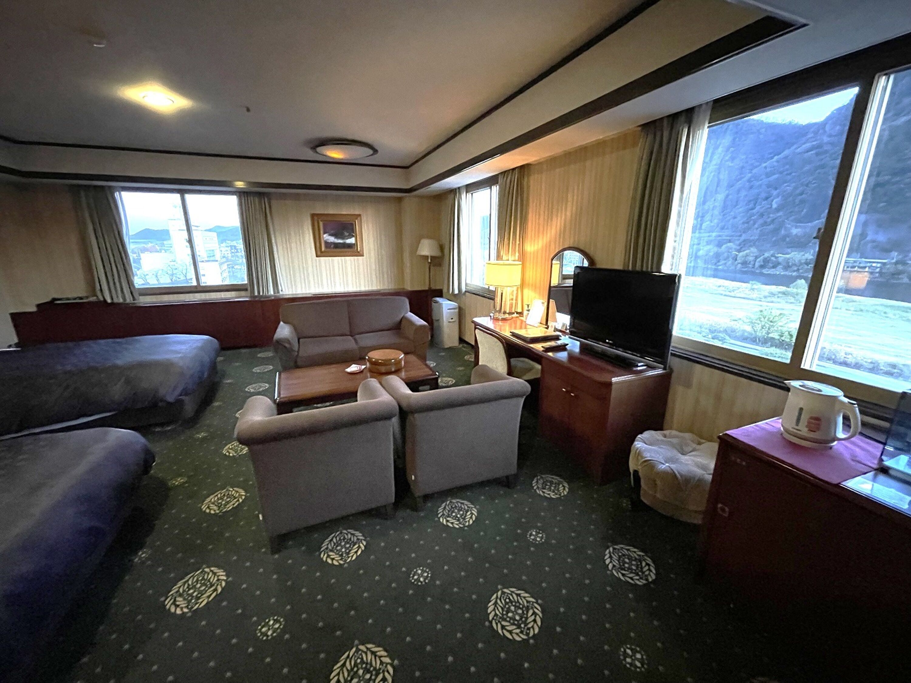 Habitación de hotel con sofá, sillones, una mesita, televisor y ventana con vistas al exterior.