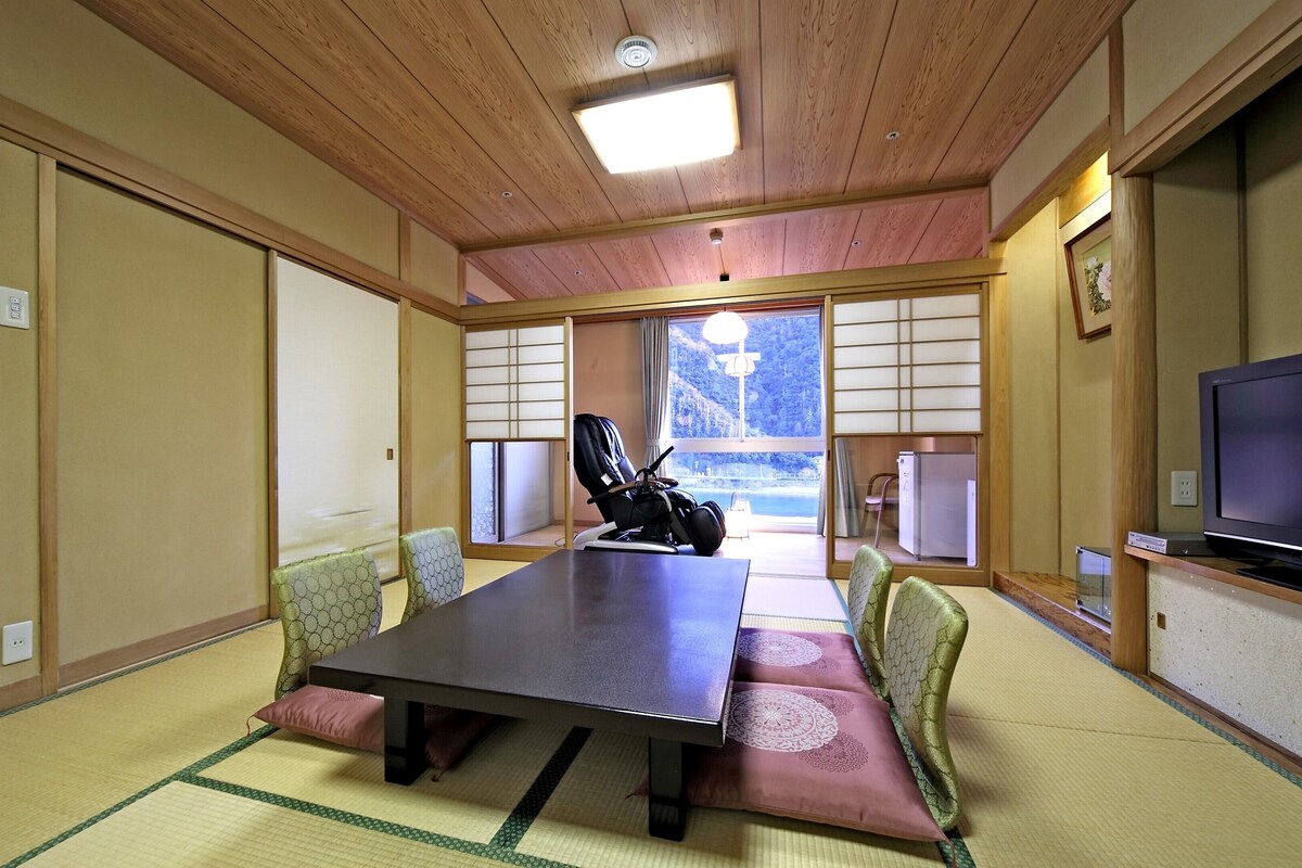 Et traditionelt japansk værelse med tatamigulv, et lavt bord og et fjernsyn på et træstel.