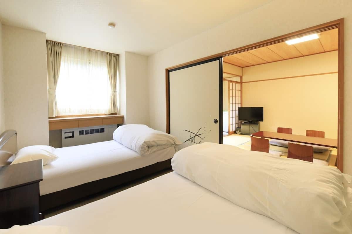 Une chambre d’hôtel comprenant un lit, un bureau avec une chaise, une télévision et une porte coulissante donnant sur une pièce de style japonais traditionnel.