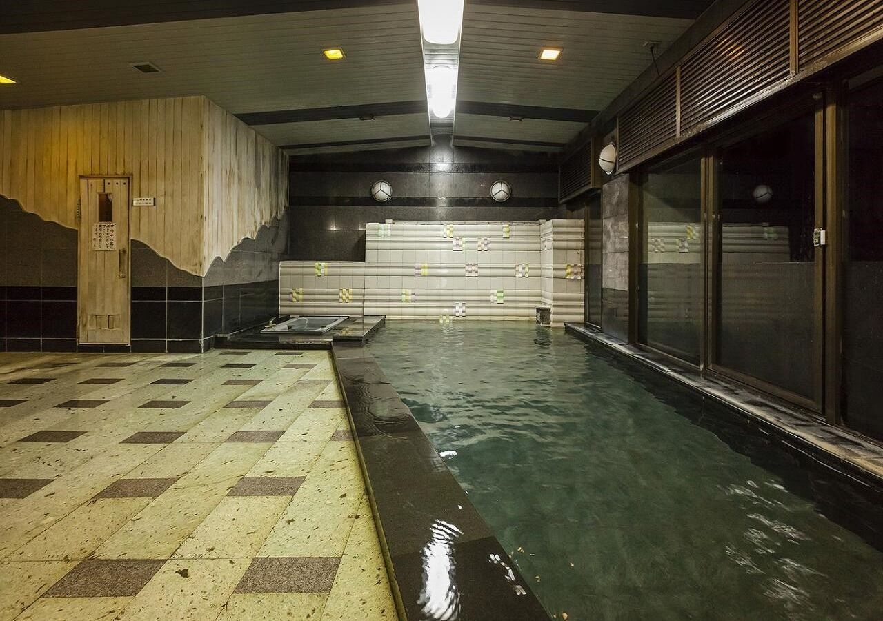An indoor swimming pool with tiled flooring, a wooden wall, and a ceiling with recessed lighting.