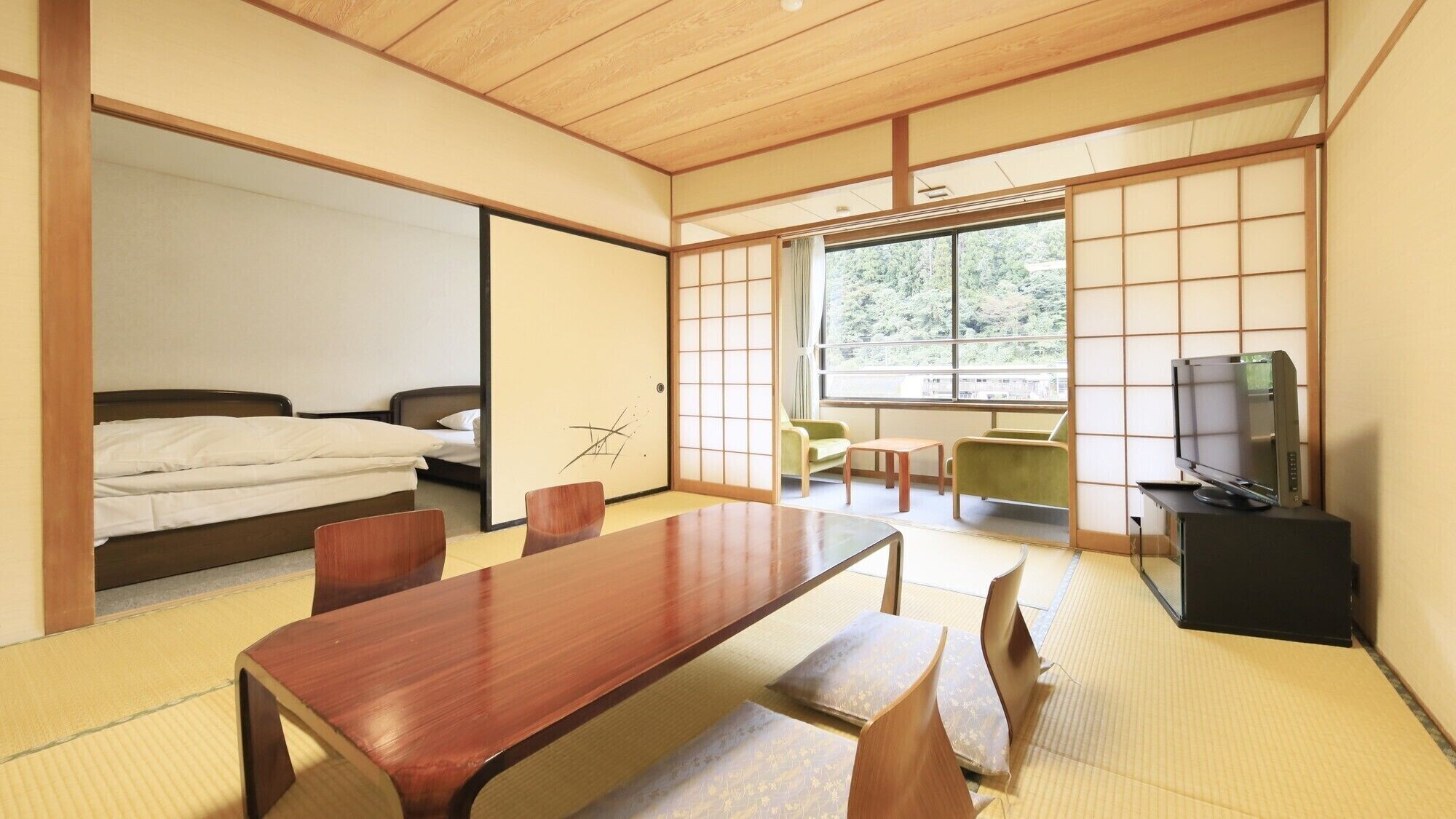 A traditional Japanese room with tatami flooring, a low table, a bed, a TV, and sliding doors.