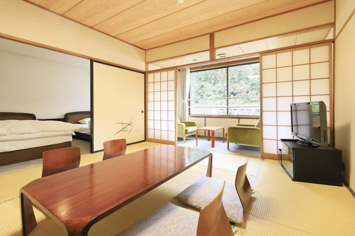 Une pièce de style japonais traditionnel, avec un sol recouvert de tatamis, une table basse, un lit, un téléviseur et des portes coulissantes.